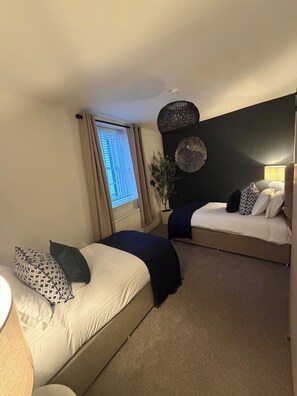 Un dormitorio con dos camas, una ventana con cortinas, una lámpara de pared y una planta en maceta.