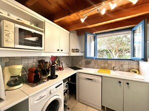 Une cuisine compacte équipée d’un lave-linge, d’une machine à café et d’une fenêtre donnant sur les arbres.