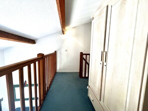 Un couloir avec une rambarde en bois, une grande armoire blanche et une moquette verte.
