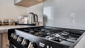 A kitchen with a gas stove, a kettle, and a toaster. - Primrose Valley 3-Bed Caravan, Sleeps 8, Pets Ok (Filey)