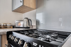 A kitchen with a gas stove, a kettle, and a toaster. - Primrose Valley 3-Bed Caravan, Sleeps 8, Pets Ok (Filey)