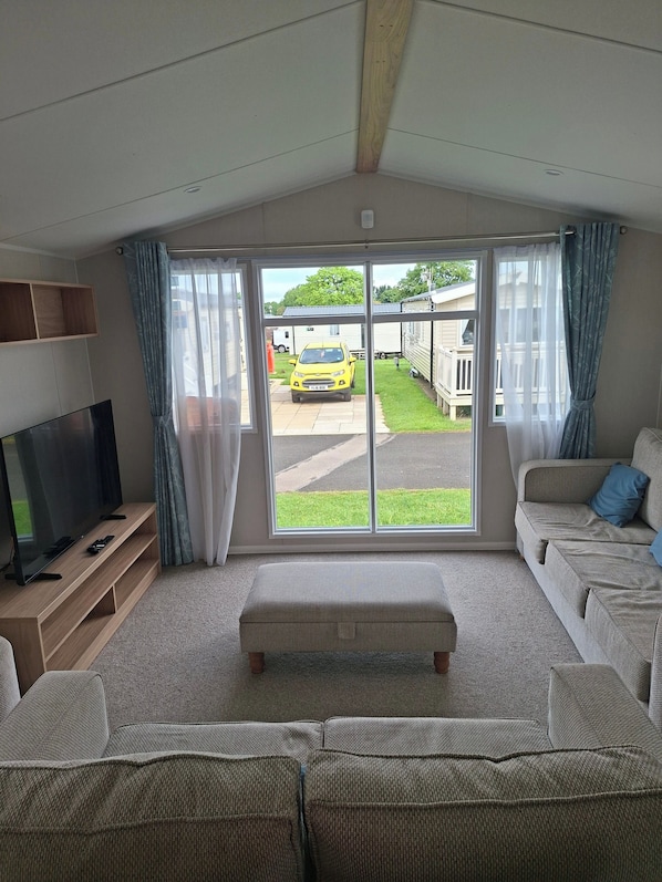 Ein Wohnzimmer mit Fernseher, Sofa, Hocker und Blick auf einen gelben Wagen draußen.