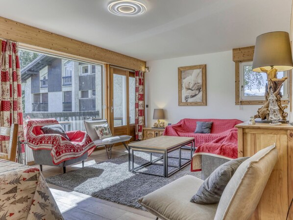 A cozy living room with a sofa, armchair, and coffee table, large windows with curtains, and a framed picture on the wall. - Spacious apartment, Mont-Blanc view - 6 guests (Megève)