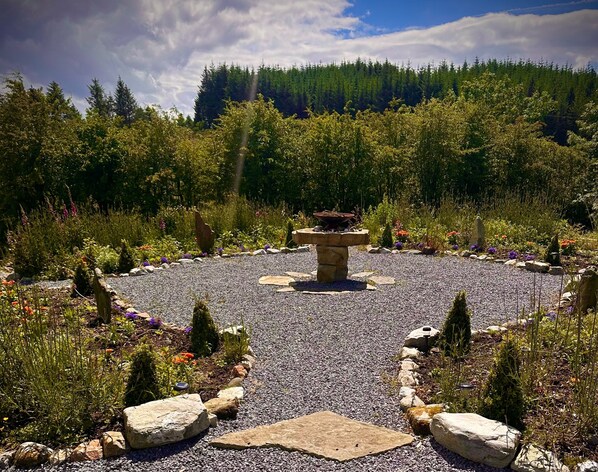 A garden with a central stone structure, surrounded by gravel and various plants.