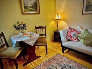 A dining area with a table set for two, a sofa, and a lamp.