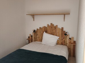 Ein Bett mit Holz-Kopfteil, einem weißen Kissen und einer grünen Decke.