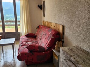 Ein Zimmer mit einem Sofa mit Holz-Kopfteil, einem kleinen Tisch, einer Lampe und Blick durch eine Schiebetür.