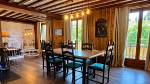 A dining area with a wooden table and chairs, a chandelier, and a view of greenery outside. - Spacious apartment with south balcony - 7 guests (Villard-de-Lans)