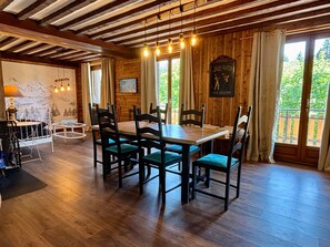Ein Essbereich mit Holztisch und Stühlen, einem Kronleuchter und Blick auf Grünflächen.