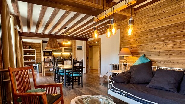A cozy living room with wooden beams, a sofa, chairs, a glass coffee table, and a dining area with a table and chairs. - Spacious apartment with south balcony - 7 guests (Villard-de-Lans)