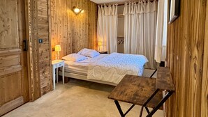 A room with wooden walls, a bed with white bedding, a bedside table with a lamp, and a small wooden table. - Spacious apartment with south balcony - 7 guests (Villard-de-Lans)