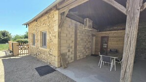 Ein Steinhaus mit überdachter Terrasse, einem Metallgitter und einem Tisch mit Stühlen.