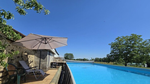 Eine Holzterrasse mit Pool, Liegestühlen und Sonnenschirm.