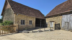 Ein Steinhaus mit Ziegeldach, ein von Zäunen umgebenes Gebiet mit Topfpflanzen und ein Holztor.