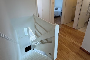 Een trap met witte leuningen, houten vloer en een deur die leidt naar een slaapkamer met een bed.