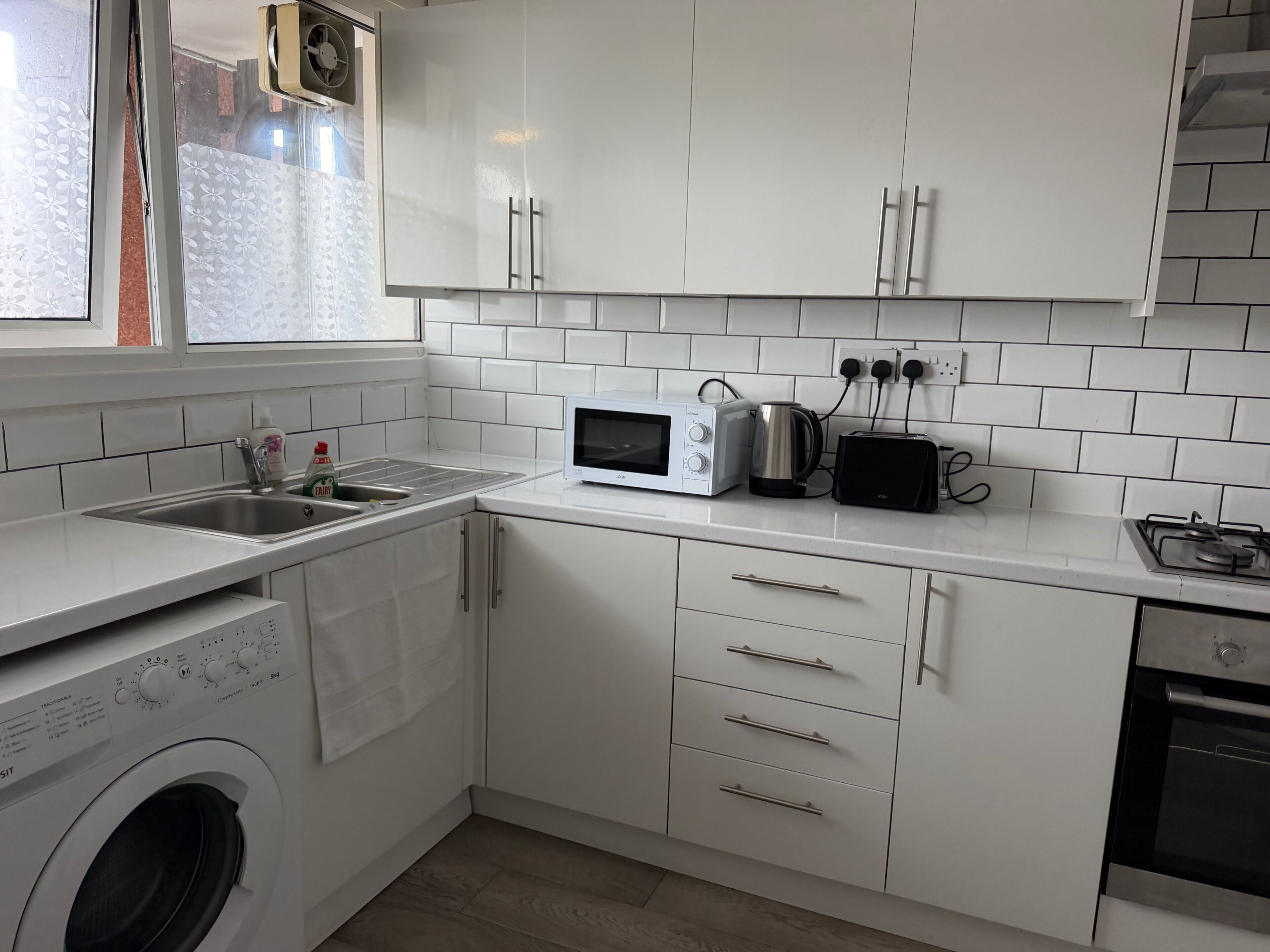 A modern kitchen with white cabinets, a built-in washing machine, a microwave, a toaster, and a gas stove.. Apartment Sleeps 6 - Wifi & Free Parking