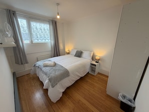 A bedroom with a bed, bedside lamps, a window with curtains, a ceiling light, and a wooden floor.