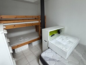 Un llit superposat amb un escriptori i una petita estant, una paret blanca i un terra amb rajoles.