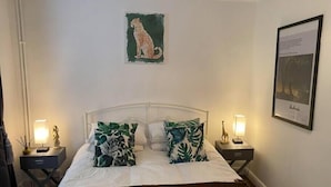 Een bed met witte beddengoed, twee nachtkastjes met lampen, een ingelijst beeld aan de muur en een schilderij van een luipaard.