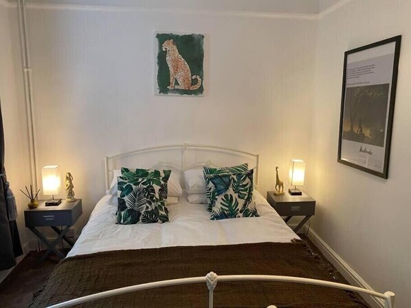 Ein Bett mit weißer Bettwäsche, zwei Nachttische mit Lampen, ein gerahmtes Bild an der Wand und ein Gemälde von einem Leopard.