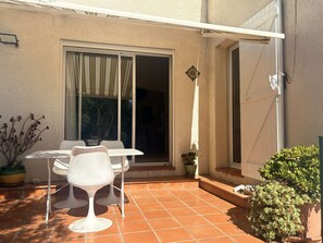 Eine Terrasse mit Tisch und Stühlen, eine Glasschiebetür und Kübelpflanzen.