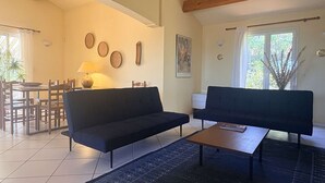 Ein Wohnzimmer mit zwei Sofas, einem Couchtisch, einem Esstisch mit Stühlen, einer Lampe und einem Bild an der Wand.