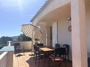 Eine Außenpatio mit Tisch und Stühlen, einem gestreiften Sonnenschirm und Blick auf die Landschaft.