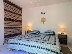 Ein Schlafzimmer mit gestreiftem Bettbezug, zwei Nachttischlampen, einem Wandventilator und einem dekorativen Wandbild.