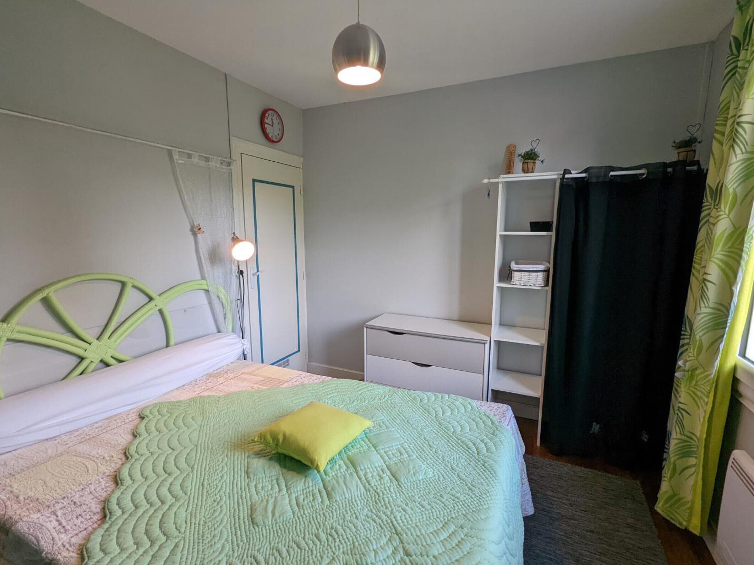 A bedroom with a bed, a desk, a chair, a wardrobe, a clock, and a window with curtains.