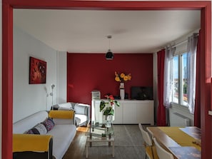 Uma sala de estar com sofá, mesa de centro com plantas, televisão e uma parede em destaque vermelha.