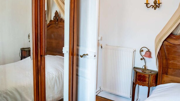 Une chambre à coucher avec un lit en bois, un miroir, un radiateur et un luminaire fixé au mur.