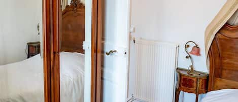 A bedroom with a wooden bed, a mirror, a radiator, and a wall-mounted light fixture.