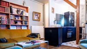 Un salon comprenant un canapé, une table basse, une bibliothèque et un coin cuisine avec des placards et des appareils électroménagers.