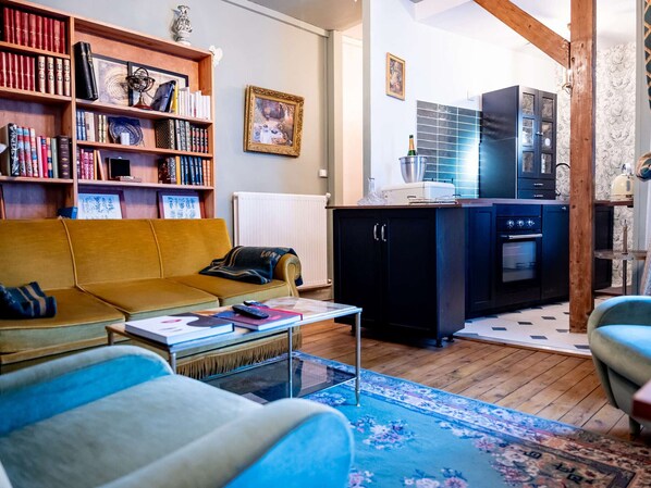 A living room with a sofa, a coffee table, a bookshelf, and a kitchen area with cabinets and appliances.