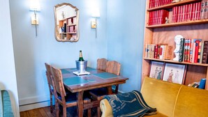 Un coin repas avec une table en bois, des chaises, une bouteille de champagne et une bibliothèque contenant des livres et des objets décoratifs.