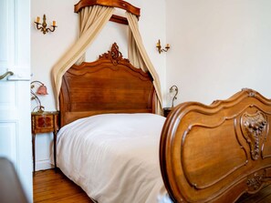 Een slaapkamer met een hemelbed van hout, een nachtkastje met een lamp en een wandlamp.