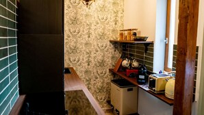 Une cuisine de taille réduite, avec un papier peint à motifs, un luminaire suspendu et des appareils électroménagers d’époque.