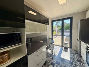 Una cocina moderna con microondas, hervidor y comedor con una silla.