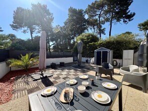 Eine Terrasse im Freien mit einem Esstisch, umgeben von Stühlen, einem Sonnenschirm und einem kleinen Schuppen.