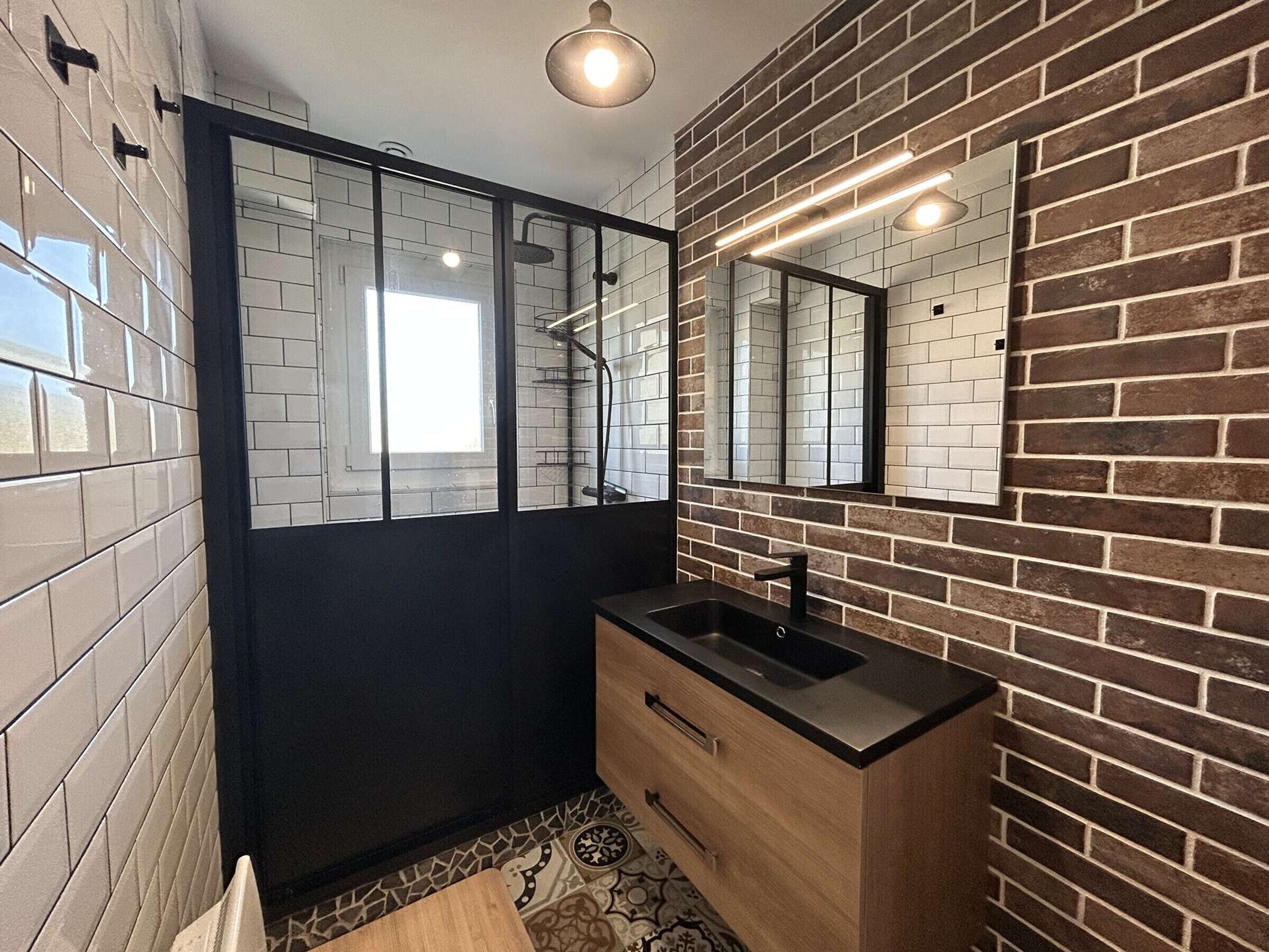 A modern bathroom with a black door, a wooden vanity, a mirror, and a shower area.