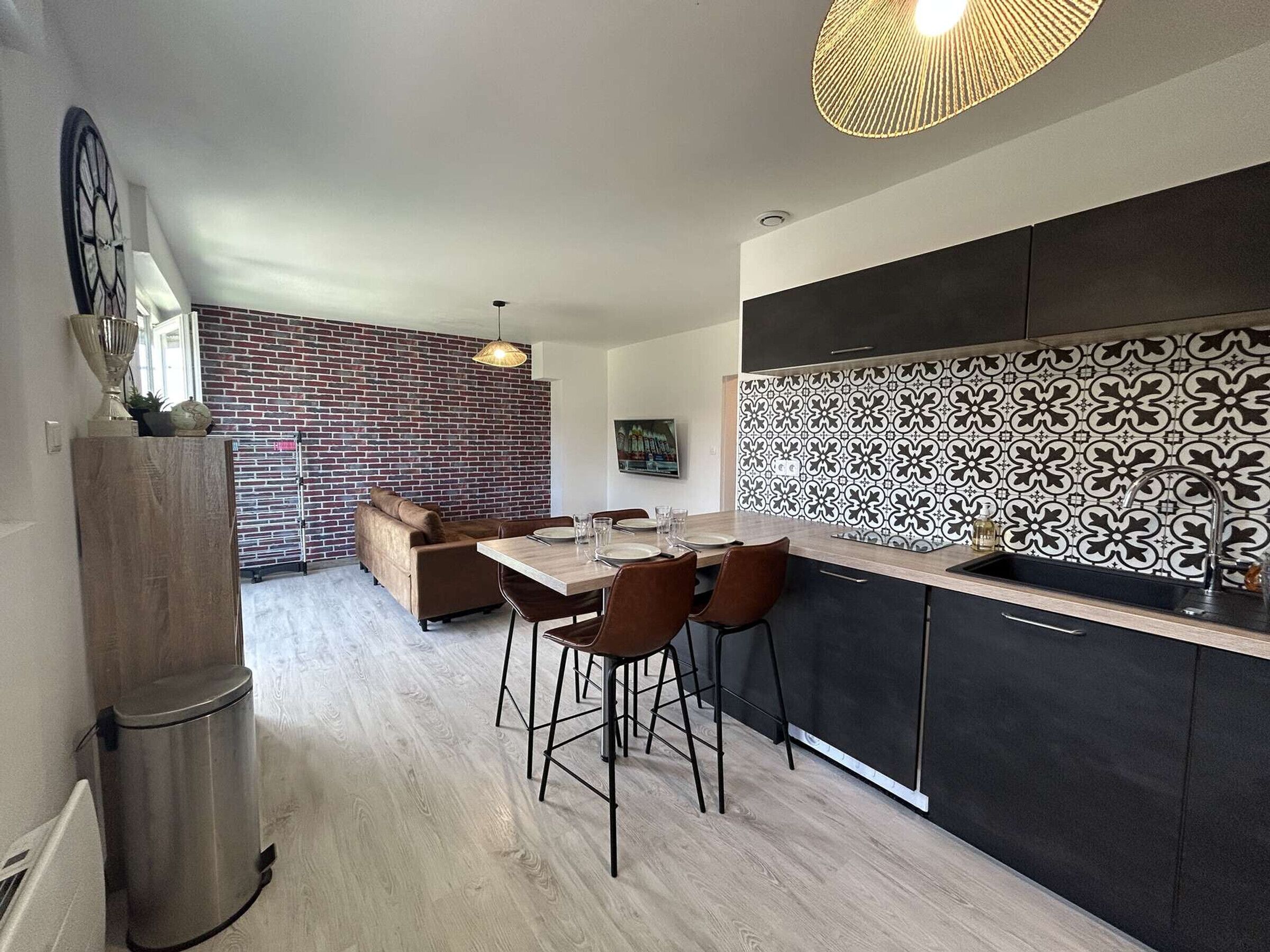 Eine moderne Küche mit schwarzem und weißem Fliesenrückwand, einem Essbereich mit Holztisch und -stühlen sowie einer Ziegelwand.