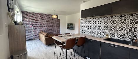Une cuisine moderne avec un mur recouvert de carreaux noirs et blancs, un coin repas avec une table et des chaises en bois, et un mur en briques.