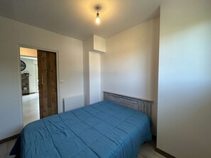 A bedroom with a bed, a wooden door, and a light fixture. - Bright apartment near the sea - 4 guests (La Barre-de-Monts)
