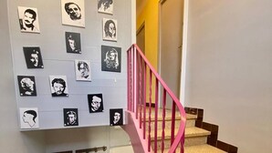 Eine Treppe mit rosafarbenen Geländern und einer Wand mit Schwarz-Weiß-Porträts.