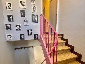Eine Treppe mit rosafarbenen Geländern und einer Wand mit Schwarz-Weiß-Porträts.