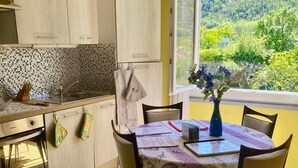 Eine Küche mit Esstisch, Stühlen, einem Fenster mit Blick auf Grünflächen und einer Blumenvase.