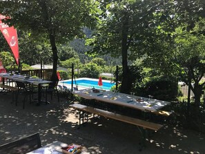 An outdoor dining area with tables and chairs, a pool, and trees in the background. - Cozy mobile home - 4 guests (Vesseaux)