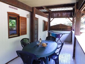 Uma área de refeições coberta ao ar livre, com mesa, cadeiras, uma garrafa e uma cesta.