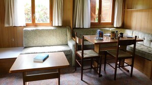 Ein gemütliches Blockhaus-Interieur mit Esstisch, zwei Holzstühlen, einer Bank und einem Sofa.