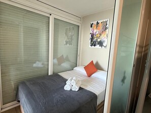 Ein Hotelzimmer mit Bett, Fenster mit Jalousien, Wandbild und Tür.